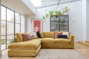 Wadenhoe corner sofa in Portland Brass velvet with natural daylight shining in the window behind it