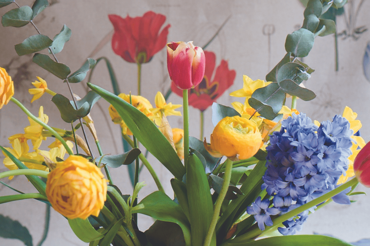 An arrangement of spring flowers, including tulips and lilac, against a floral fabric background.