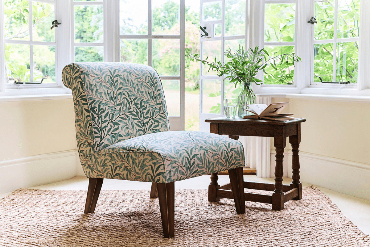 An occasion chair in William Morris Willow Bough fabric, accompanied by a small table with a book, glass of water and vase of flowers